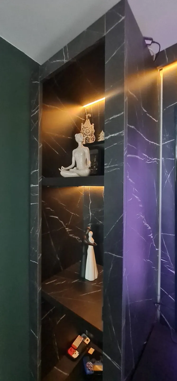 Media wall alcove with black marble-effect panels and warm-lit shelves